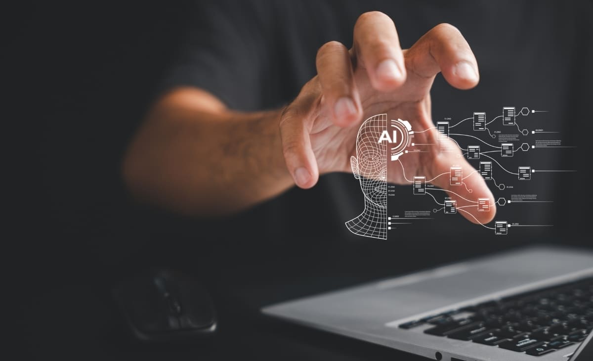 An image of a persons hand holding a digitalised person with the words AI written on them, showcasing how AI has become a vital part of modern work environments.